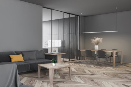 Corner of modern living room with gray walls, wooden floor, comfortable gray sofa with round coffee table and stylish long gray dining table in background. 3d rendering