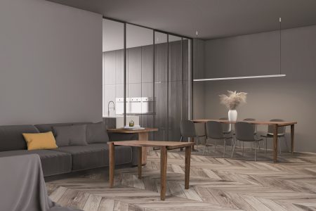 Corner of modern living room with gray walls, wooden floor, comfortable gray sofa with round coffee table and stylish long gray dining table in background. 3d rendering